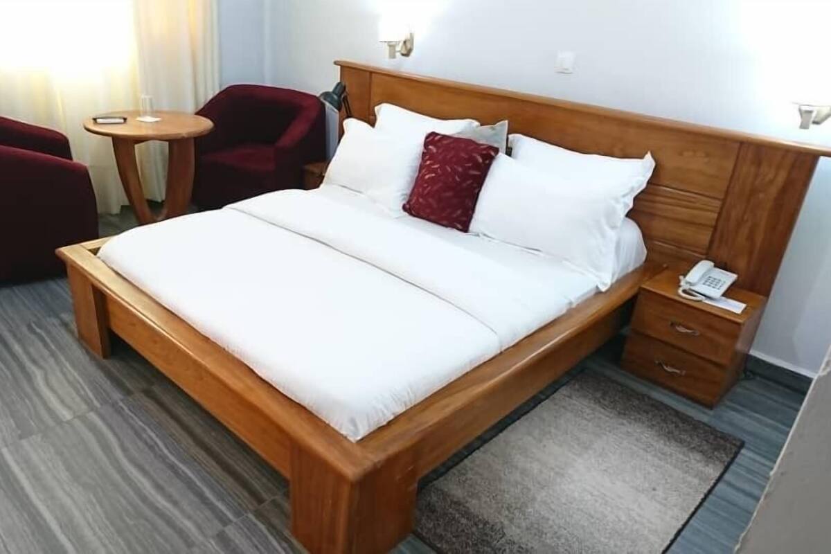 Ein Hotelzimmer mit einem hölzernen Bett, einem kleinen runden Tisch, einem roten Sessel und einem Nachttischtelefon.