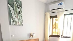 Habitación de hotel con cama de madera, una silla roja, una mesita redonda y aire acondicionado instalado en la pared.