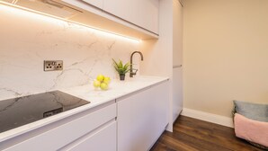 A modern kitchen with a white marble countertop, a black induction cooktop, a built-in oven, and a small potted plant.