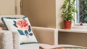 A beige armchair with a floral pillow, a small potted plant, and a window with a view of greenery.