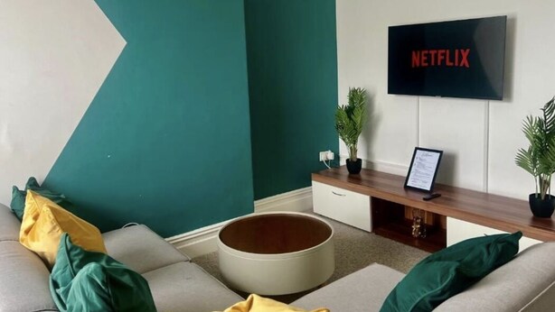 A living room with a sofa, a round coffee table, a TV mounted on the wall, and a small plant on the side table.