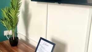 A wooden reception desk with a framed welcome sign, a potted plant, and a remote control. A large TV screen above displays the Netflix logo.