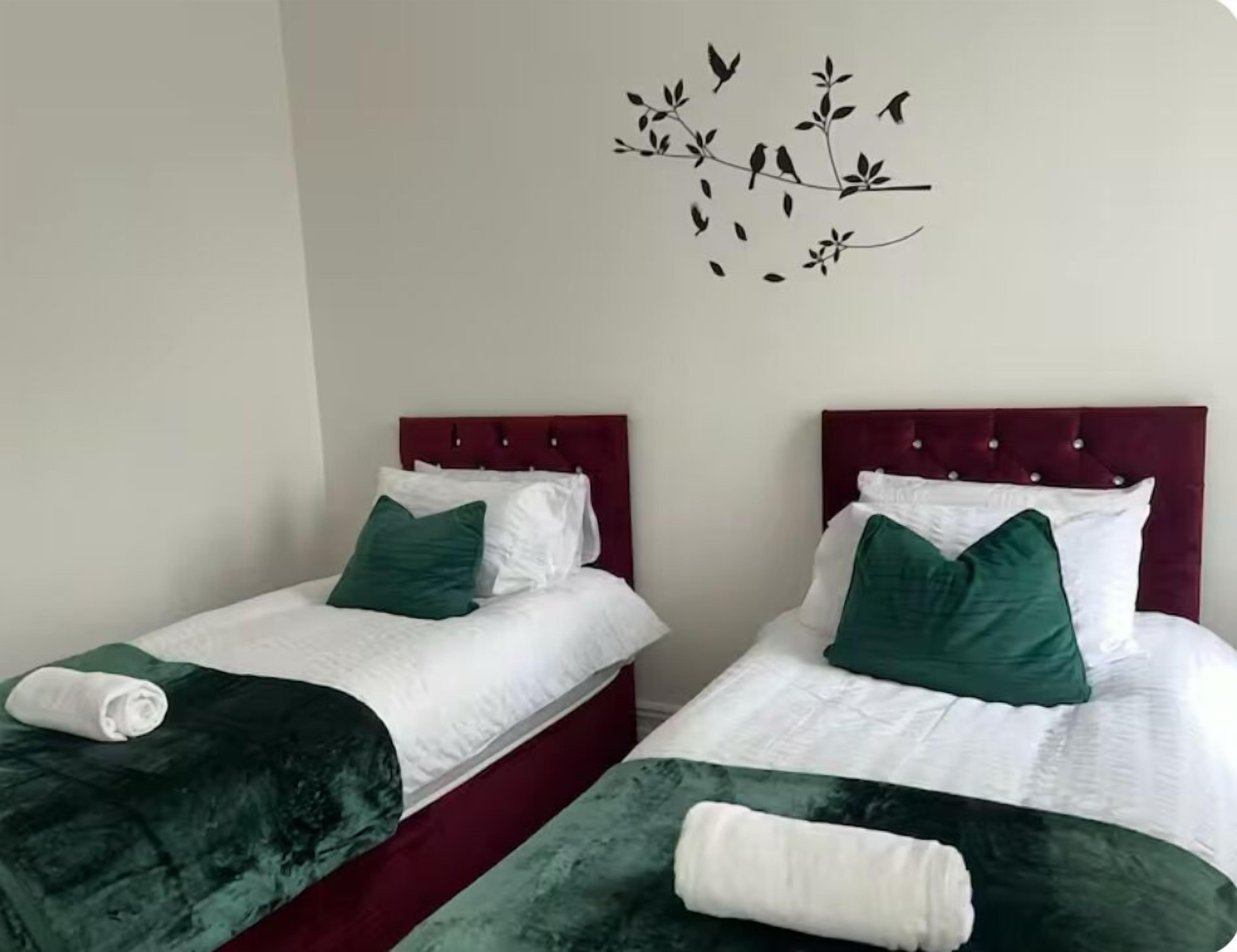 Two single beds with red headboards, white bedding, and green pillows.