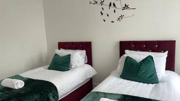 Two single beds with red headboards, white bedding, and green pillows.