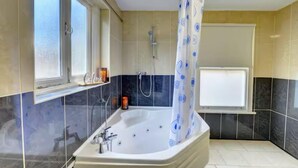 A bathroom with a large bathtub, a shower, and a window with a curtain.