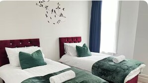 Two twin beds with green and white bedding, a red headboard, and a wall art piece above them.