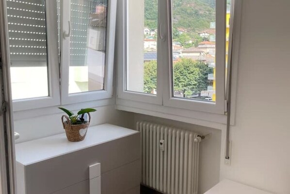 A room with a white radiator, a window with blinds, and a small plant on a shelf. - Mia Apartment (Lavis)