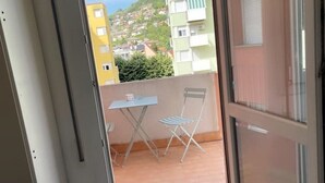 A balcony with a table and chairs, a view of a hillside with buildings, and a door leading into the room. - Mia Apartment (Lavis)