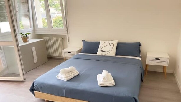 A modern bedroom with a large bed, two bedside tables, and a view of greenery outside. - Mia Apartment (Lavis)