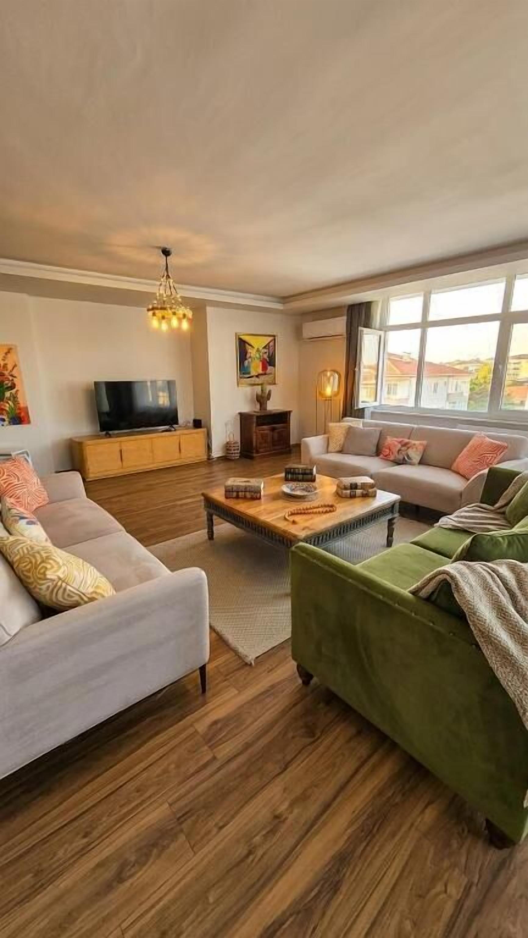 A living room with a sofa, a green armchair, a wooden coffee table, a TV, and a painting on the wall.