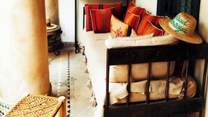 A cozy room with a sofa, a woven chair, a table with a painting, and a decorative hat. - Privatized Riad in the authentic medina of Marrakech (Marrakech)