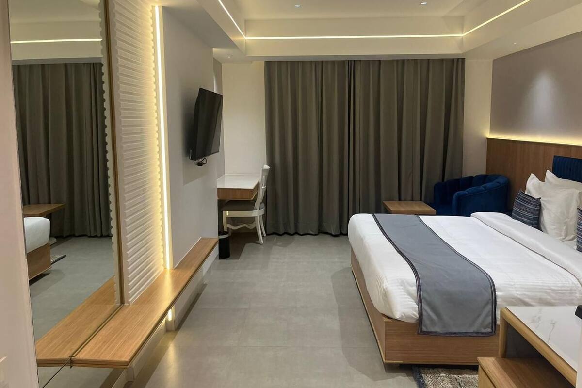 A modern hotel room with a large bed, a desk, a chair, and a TV.