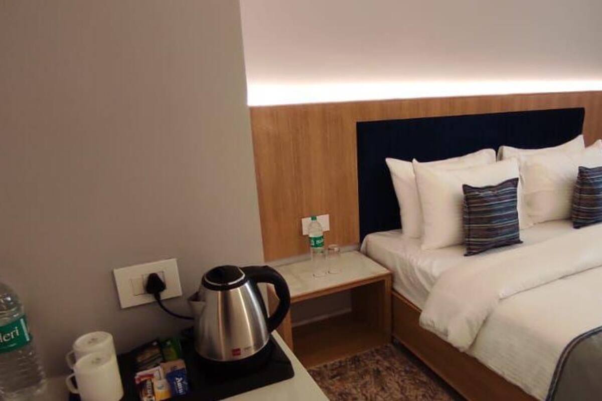 A hotel room with a bed, bedside table, and a nightstand with a kettle and a bottle of water.