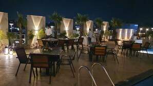 An outdoor dining area with tables and chairs, palm trees, and ambient lighting. - Sapphire Blue (Bhopal)
