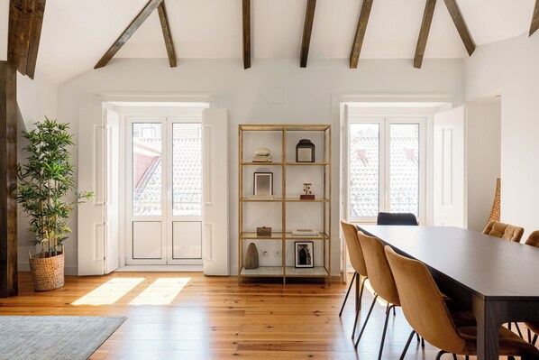 A room with wooden floors, a dining table with chairs, a bookshelf, and a potted plant.