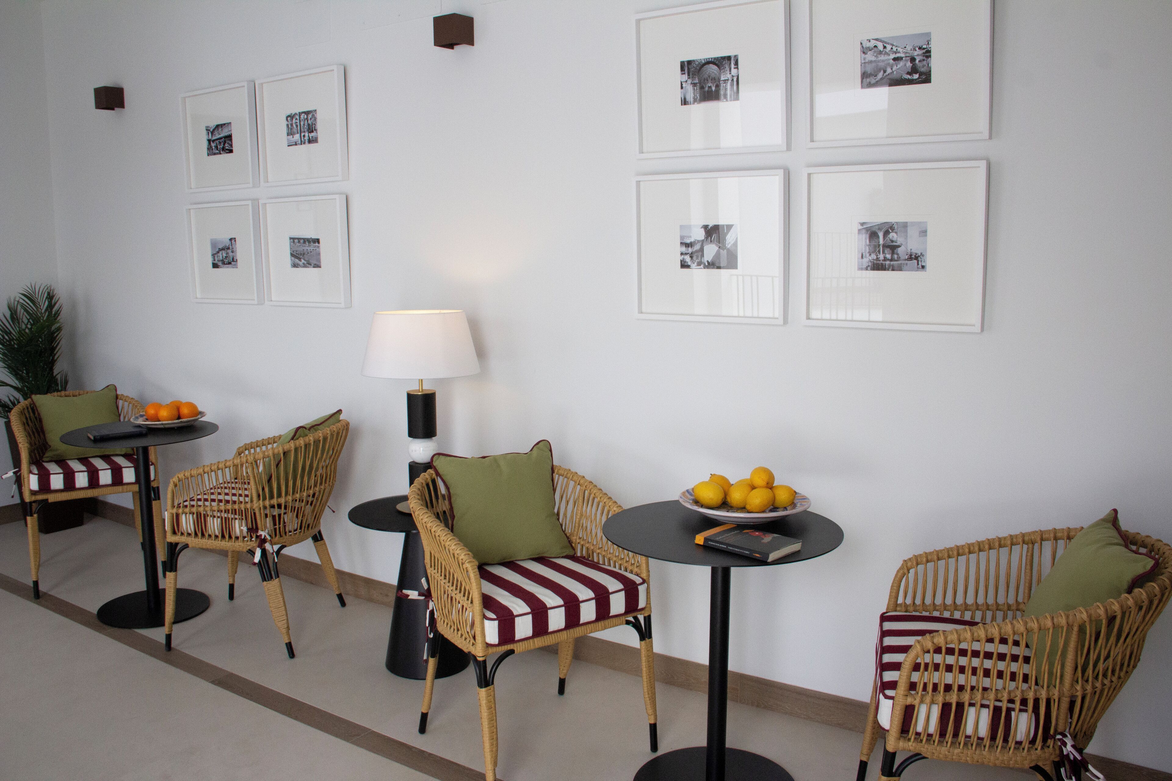 A room with wicker chairs, a round table with a lamp, and framed pictures on the wall.