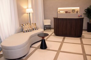 A modern reception area with a curved sofa, a small round table, a reception desk, and a lamp. - Puerta de la Ribera Suites (Córdoba)