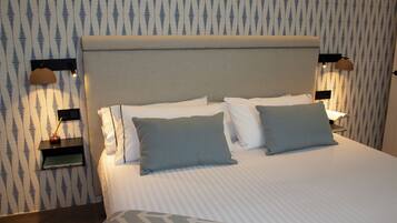 A neatly made bed with a patterned bedspread, two bedside tables with lamps, and a wall with a striped wallpaper pattern.