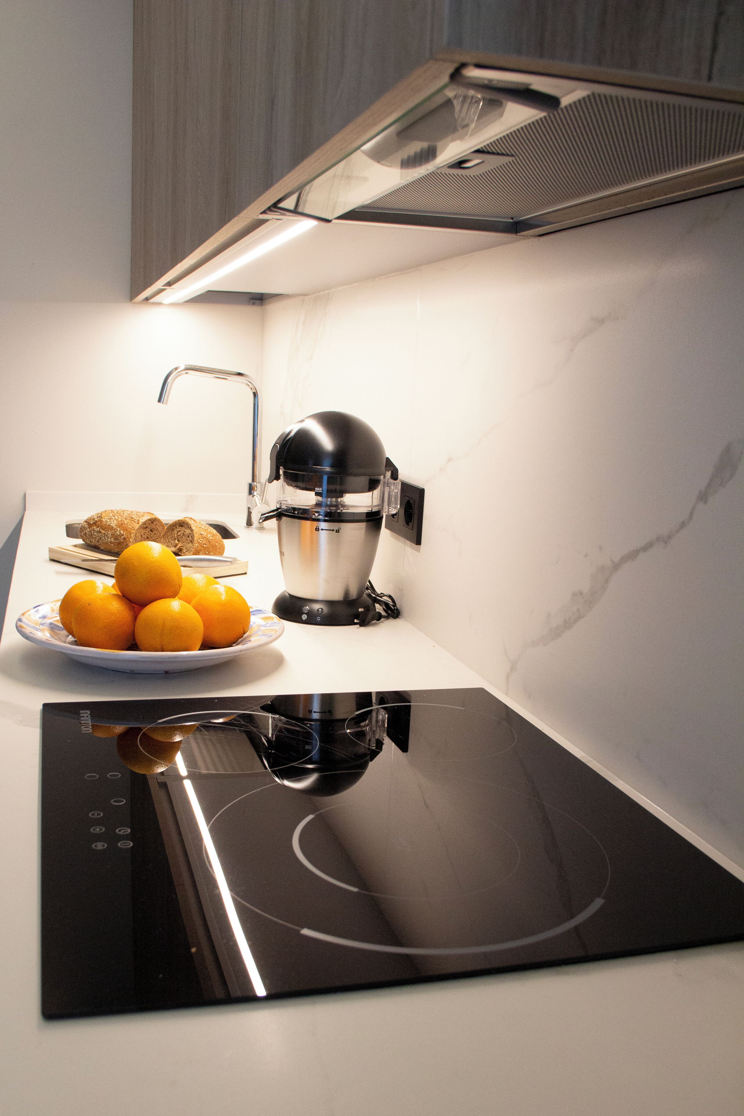 Una cocina moderna con una placa de inducción integrada, un exprimidor y un plato de naranjas.