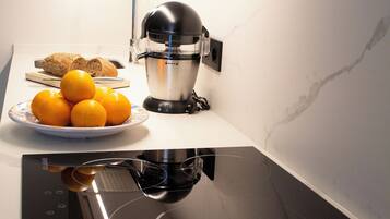 Una cocina moderna con una placa de inducción integrada, un exprimidor y un plato de naranjas.