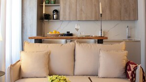 A cozy living room with a wooden ceiling, a sofa, a coffee table, and a kitchen area in the background. - Puerta de la Ribera Suites (Córdoba)