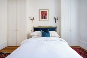 A bedroom with a bed, white walls, a framed picture, and a red patterned rug. - Highlife and Islington - by Out of Office Lifestyle (Greater London)