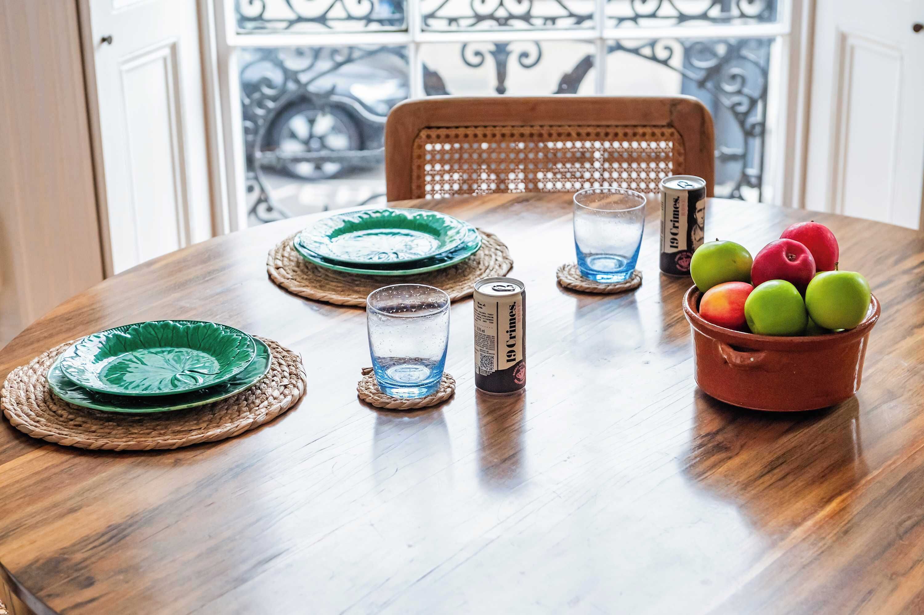 Una mesa de madera con platos verdes, una copa, una lata y un cuenco de manzanas.