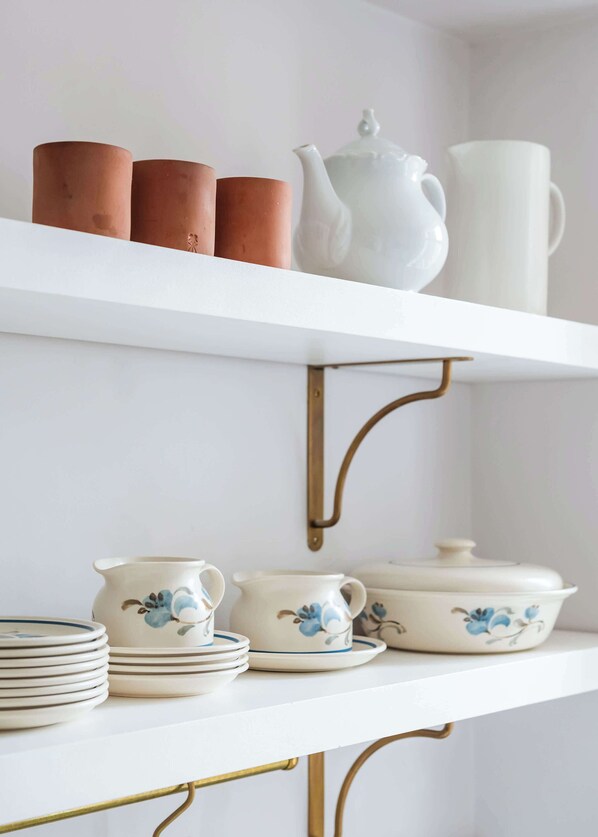 A white shelf with a white teapot, three brown cups, and a white pitcher. Below, there are white plates with blue floral designs and a white teapot with a lid.