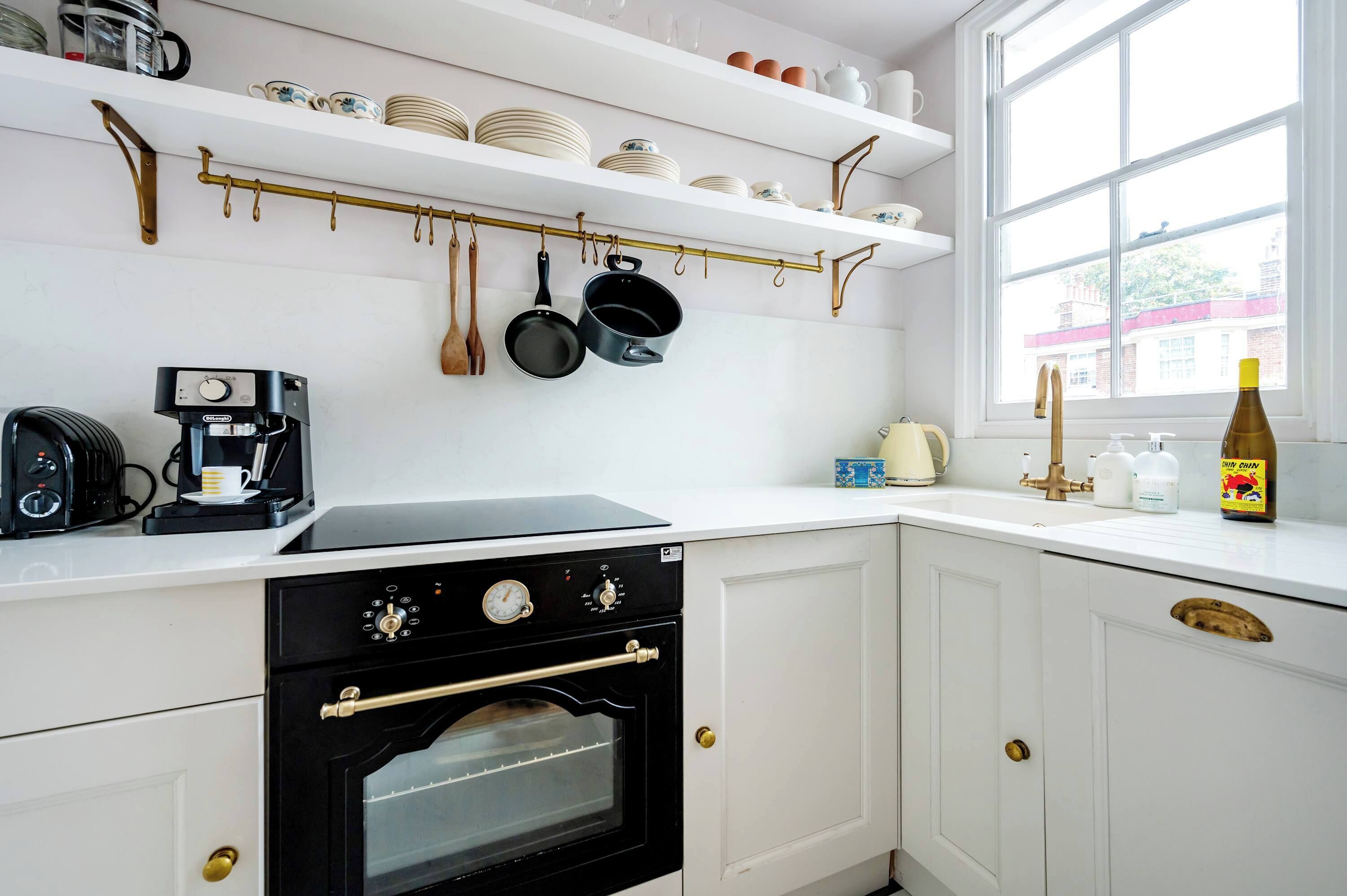A kitchen with white cabinets, a stove, a coffee maker, and hanging utensils.