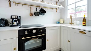 A kitchen with white cabinets, a stove, a coffee maker, and hanging utensils. - Highlife and Islington - by Out of Office Lifestyle (Greater London)