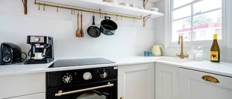 A kitchen with white cabinets, a stove, a coffee maker, and hanging utensils.
