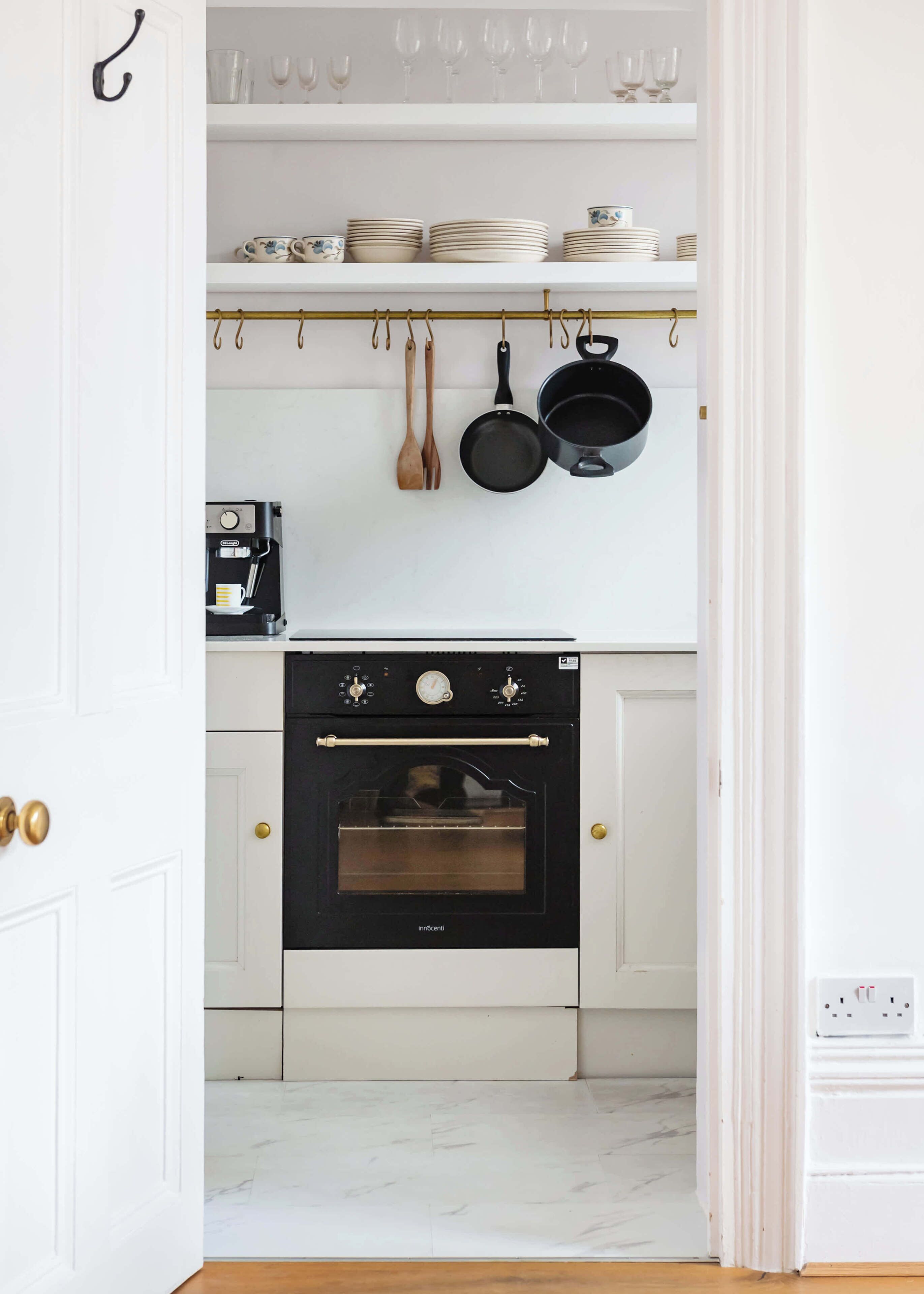 A kitchen with white cabinets, a black oven, and hanging utensils.