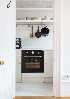 A kitchen with white cabinets, a black oven, and hanging utensils.