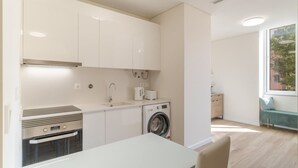 A modern kitchen with white cabinets, a built-in oven, a washing machine, and a dining area with a table and chairs. - Carmo Palace I in Funchal (Funchal)
