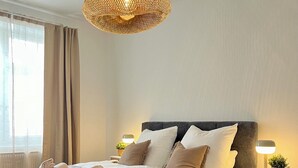 Una cama bien hecha con una colcha acolchada, dos lámparas de noche y una lámpara decorativa colgante.