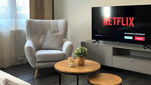 Una sala de estar moderna con un sofá gris, una mesa de centro redonda, un televisor mostrando el logo de Netflix y una lámpara colgante original.