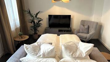 Ein Hotelzimmer mit einem Bett, einem Fernseher, einem grauen Sessel, einem kleinen Tisch und einer Topfpflanze.