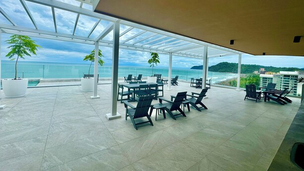 A spacious outdoor seating area with tables and chairs, overlooking a beach and ocean. - New Ocean View Beach Front Deluxe Condo! (Jaco)
