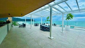 A spacious outdoor terrace with a glass roof, overlooking a beach and ocean. - New Ocean View Beach Front Deluxe Condo! (Jaco)