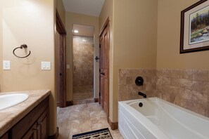 A bathroom with a white bathtub, beige walls, a wooden door, and a tiled shower area. - Peregrine Point Condo Steps to Lifts - AC/Amazing Views (Durango)
