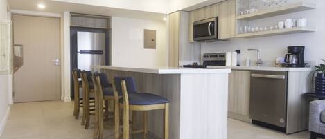 A modern kitchen with a central island, bar stools, a microwave, a coffee maker, and a dishwasher.