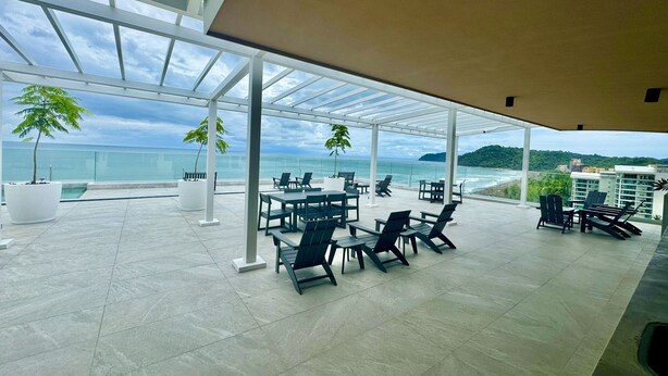 A spacious outdoor seating area with tables and chairs, overlooking a beach and ocean. - J-pacp506 3 Bedroom Condo (Jacó)
