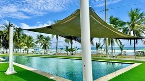 A pool area with a shaded canopy, palm trees, and a view of the beach. - J-pacp506 3 Bedroom Condo (Jacó)