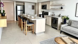 A modern kitchen with a central island, a dining area with chairs, a sofa, and a small coffee table. - J-pacp506 3 Bedroom Condo (Jacó)