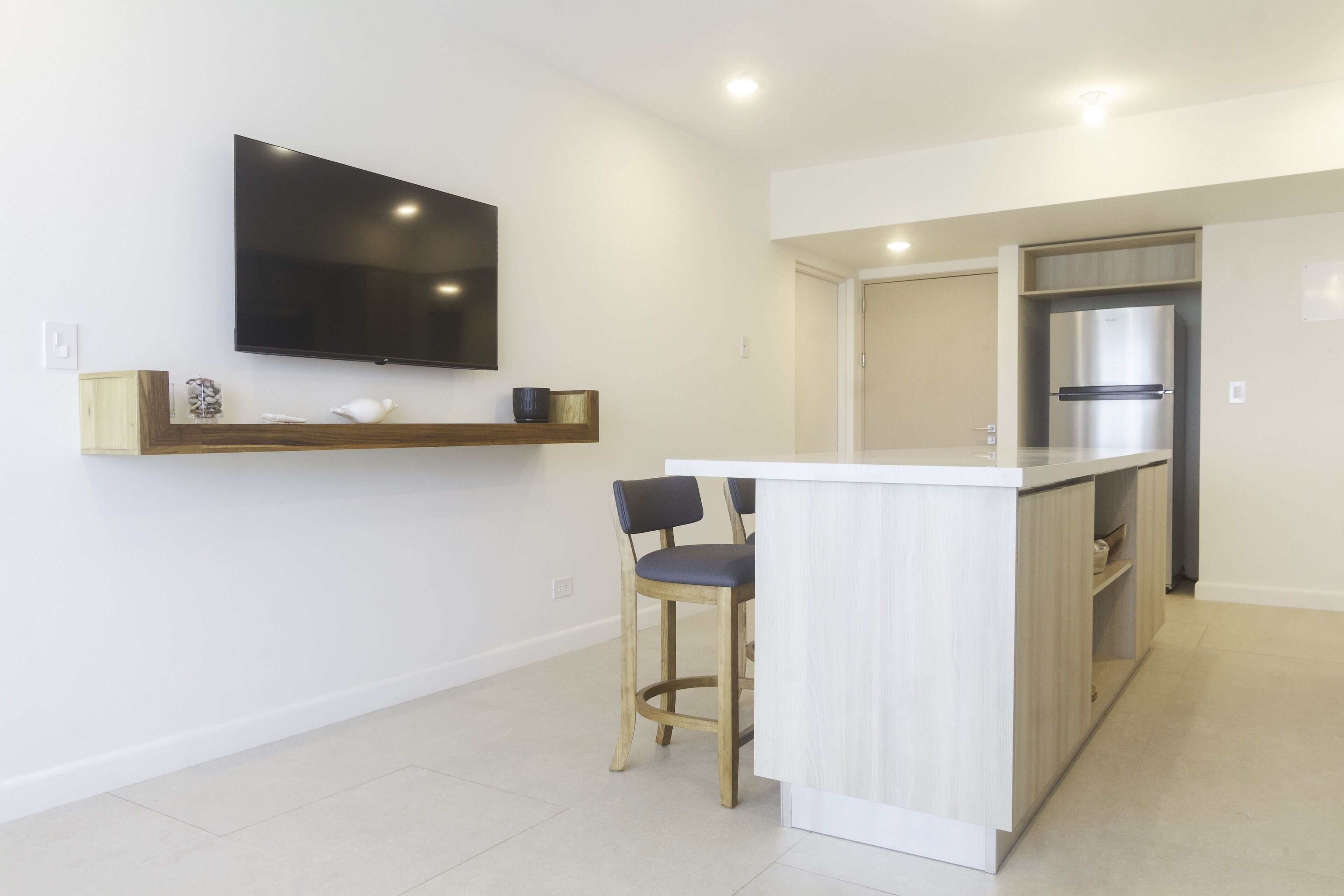 Een moderne keuken met een inbouwkookeiland, barstoelen, een flatscreen televisie en een roestvrijstalen koelkast.