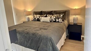A bedroom with a large bed, a nightstand with a lamp, and a wall-mounted shelf. - J-pacp506 3 Bedroom Condo (Jacó)