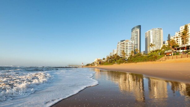 A beach with a sandy shore and ocean waves. There are high-rise buildings in the background. - Gorgeous One Bedroom Oceans (uMhlanga Rocks, KwaZulu-Natal)