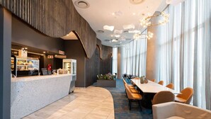 A modern hotel lobby with a reception desk, a long dining table with chairs, and a seating area with a round table and chairs. - Gorgeous One Bedroom Oceans (uMhlanga Rocks, KwaZulu-Natal)