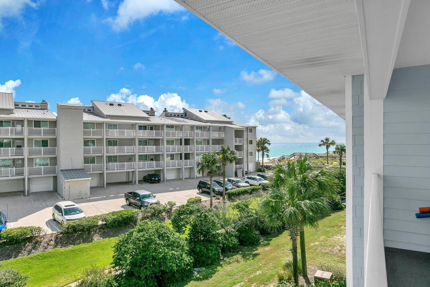 A multi-story hotel with balconies, a parking lot, and a view of the beach.