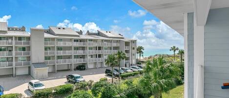 A multi-story hotel with balconies, a parking lot, and a view of the beach.
